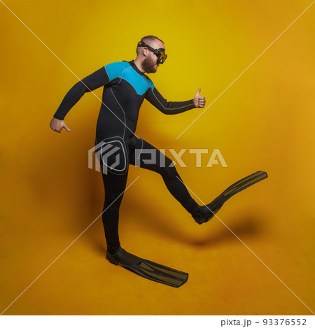 Traveling concept. Happy diver in a mask and fins going somewhere against yellow studio background 93376552