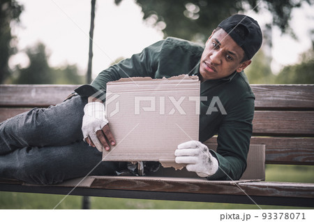 Man reclining on bench showing cardboard to camera Man reclining on bench showing cardboard to camera 93378071