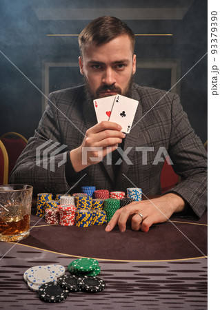 Handsome bearded man is playing poker sitting at the table in casino. 93379390