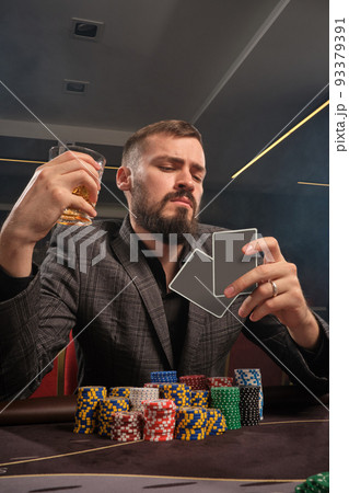 Handsome bearded man is playing poker sitting at the table in casino. 93379391