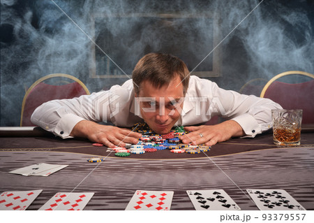 Handsome emotional man is playing poker sitting at the table in casino. 93379557