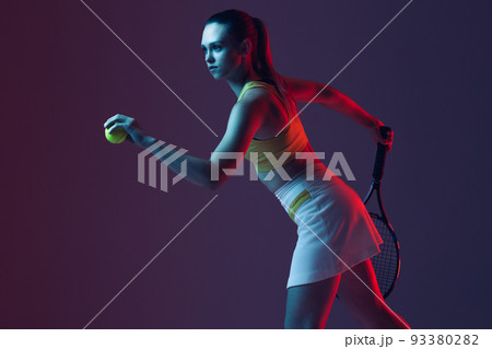 Young woman, professional tennis player training isolated on blue background in neon. 93380282