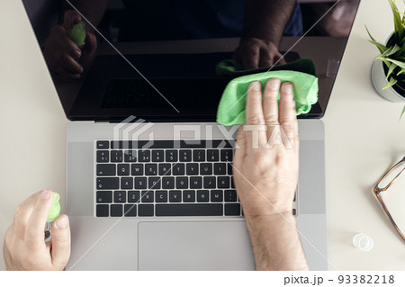 Computer cleaning concept. Top view of a male human hands cleaning a laptop screen with cleaning spray and antistatic cloth 93382218