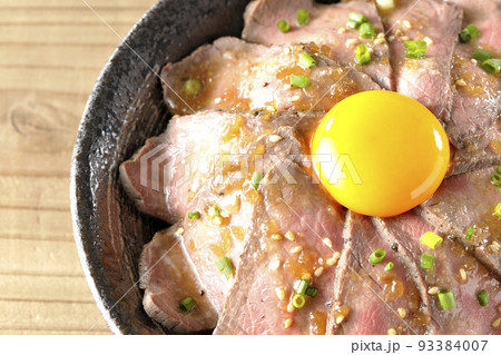 生卵の黄身と万能ねぎ、白胡麻が乗っているローストビーフ丼を俯瞰で撮影 93384007