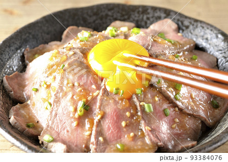 生卵の黄身と万能ねぎ、白胡麻が乗っているローストビーフ丼の卵黄を箸で割って食べる 生卵の黄身と万能ねぎ、白胡麻が乗っているローストビーフ丼の卵黄を箸で割って食べる 93384076