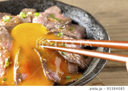 生卵の黄身と万能ねぎ、白胡麻が乗っているローストビーフ丼の卵黄を箸で割って食べる 生卵の黄身と万能ねぎ、白胡麻が乗っているローストビーフ丼の卵黄を箸で割って食べる 93384085