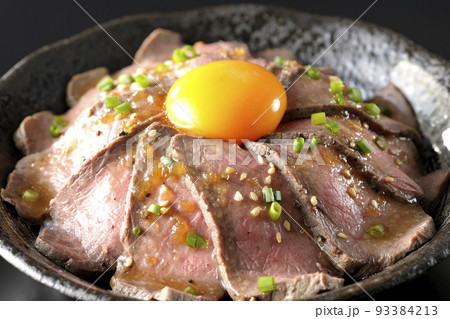 生卵の黄身と万能ねぎ、白胡麻が乗っているローストビーフ丼を黒背景で撮影 93384213