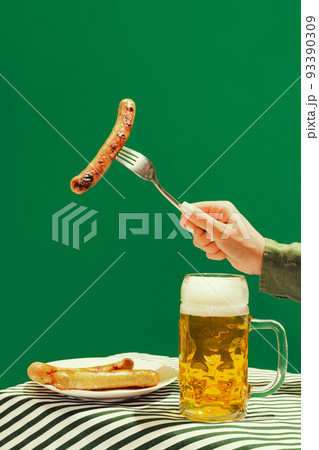 Beer and fried frankfurter. Human hand with mug of cold frothy beer over dark green background. Oktoberfest, vacation, happiness, festival and ad concept. 93390309