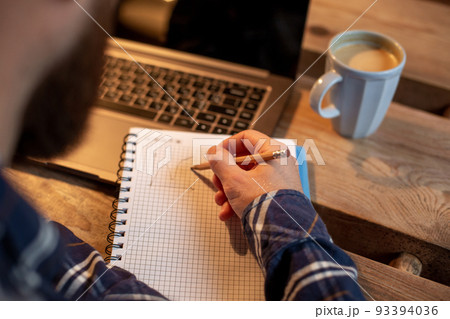 Cropped image of casual business man or freelancer planning his work on notebook, working on laptop computer with smart phone, cup of coffee on table at coffee shop or home office. Cropped image of casual business man or freelancer planning his work on notebook, working on laptop computer with smart phone, cup of coffee on table at coffee shop or home office. 93394036