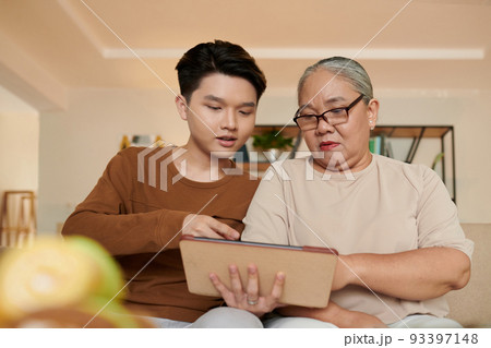Vietnamese teenage boy showing grandmother how to use tablet computer for watching her favorite shows 93397148