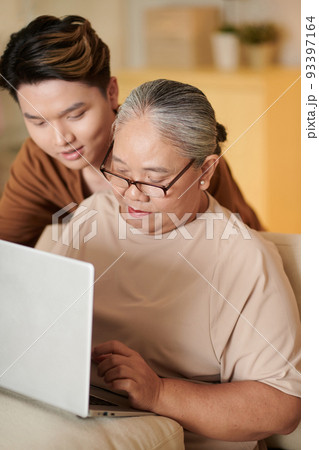 Young man teaching his grandmother how to work on laptop 93397164