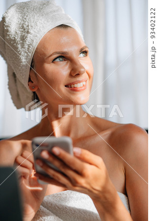Woman wrapped in a bath towel lying in bed with a laptop on her lap and holding a smartphone in her hands. Lifestyle with modern technologies. Young girl with a laptop talking on the phone and smiling Woman wrapped in a bath towel lying in bed with a laptop on her lap and holding a smartphone in her hands. Lifestyle with modern technologies. Young girl with a laptop talking on the phone and smiling 93402122