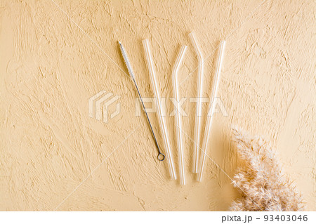 Glass reusable straws for drinks and cleaning brush on a beige textured background. Sustainable lifestyle. Top view. 93403046
