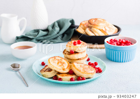 Ready-to-eat pancakes and cranberries on a plate and pan with pancakes on the table. Homemade breakfast dessert 93403247