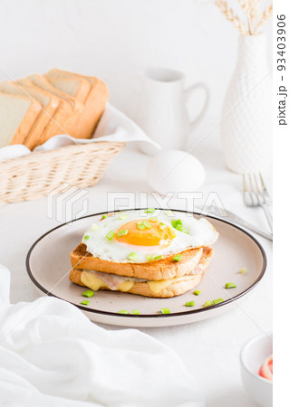 Croque madam sandwich with cheese, ham and egg on a plate on a light table. Hearty homemade breakfast. Vertical view Croque madam sandwich with cheese, ham and egg on a plate on a light table. Hearty homemade breakfast. Vertical view 93403906