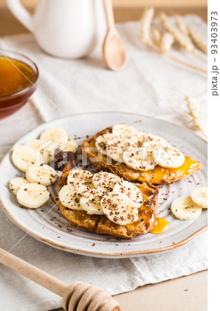 Ready to eat bruschettas with honey, banana and chocolate on a plate on the table. Vegetarian homemade snack. Vertical view Ready to eat bruschettas with honey, banana and chocolate on a plate on the table. Vegetarian homemade snack. Vertical view 93403973