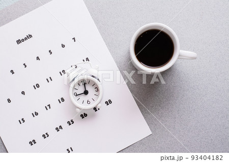 Blank sheet of monthly calendar, coffee cup and alarm clock  on a gray background. Time planning and organization. Copy space. Close-up 93404182