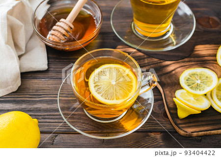 A cup of tea with a slice of lemon and a bowl of honey on a wooden table. Vitamin warming drink. Close-up 93404422