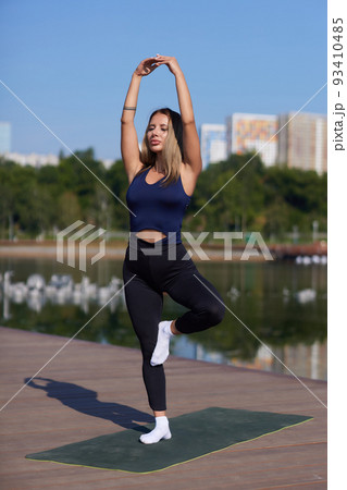 Fit young woman training on mat outdoor summer day, performing reverse plank with foam roller massager, stretching spinal muscles, doing fascia exercise. Warm-up before workouts routine, health care. 93410485