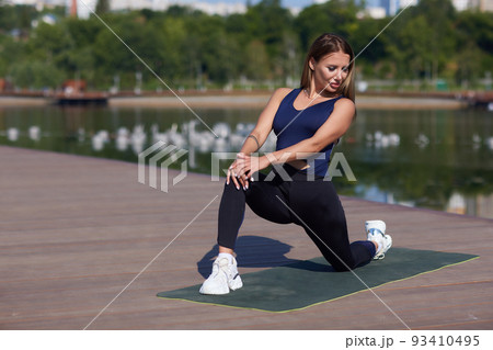 Fit young woman training on mat outdoor summer day, performing reverse plank with foam roller massager, stretching spinal muscles, doing fascia exercise. Warm-up before workouts routine, health care. 93410495