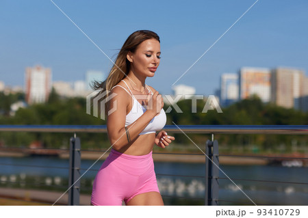 Athletic slim woman on a sunny day runs along the embankment or park. 93410729