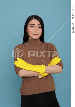 Portrait of serious confidence and satisfied asian housemaid cross hands wearing yellow gloves and cross hands isolated on a blue background, Cleaning home concept, Humble positive female standing 93410929