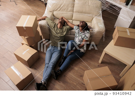 Happy partners taking break after moving in together, enjoying new beginnings in apartment flat. Sitting on living room floor and talking about future family, dreaming about achievement. Happy partners taking break after moving in together, enjoying new beginnings in apartment flat. Sitting on living room floor and talking about future family, dreaming about achievement. 93410942