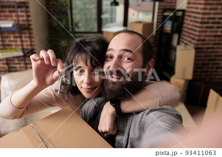 Cheerful married couple holding keys of first house bought together to move in and start new life beginnings. Showing excitement about relocation after making real estate purchase. Cheerful married couple holding keys of first house bought together to move in and start new life beginnings. Showing excitement about relocation after making real estate purchase. 93411063
