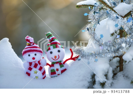 Two small funny toys baby snowman in knitted hats and scarves in deep snow outdoors near pine tree branch. Happy New Year and Merry Christmas greeting card. Two small funny toys baby snowman in knitted hats and scarves in deep snow outdoors near pine tree branch. Happy New Year and Merry Christmas greeting card. 93413788