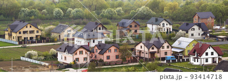 Quiet residential suburban area. Street with new modern comfortable brick cottages with yards and blooming gardens on background of beautiful green forest. Investments in real estate concept. 93414718