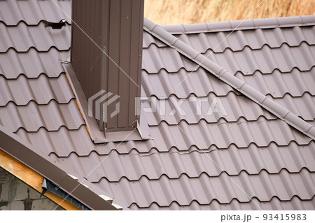 Chimney on house roof top covered with metallic shingles under construction. Tiled covering of building. Real estate development Chimney on house roof top covered with metallic shingles under construction. Tiled covering of building. Real estate development 93415983