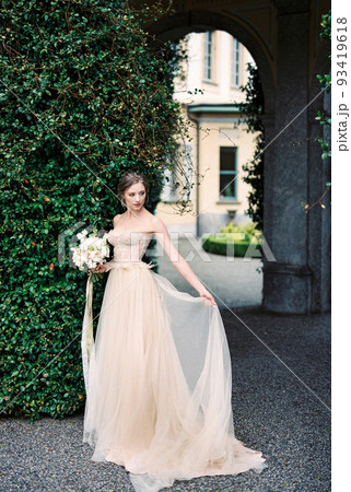 Bride with a bouquet stands near a column with green ivy 93419618