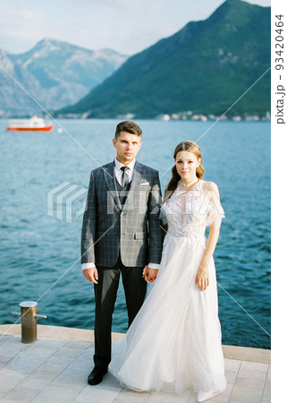 Groom holds bride hand on the pier against the backdrop of the mountains. Montenegro Groom holds bride hand on the pier against the backdrop of the mountains. Montenegro 93420464