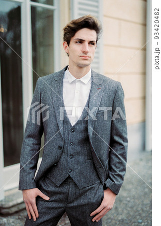 Man in a gray suit stands near the wall of an old villa with large windows 93420482