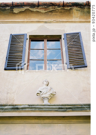 Statue on a parapet under a shuttered window on the facade of an old villa. Florence, Italy 93420775