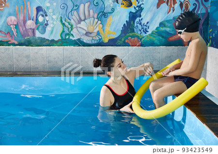 Preschool boy learning to swim in pool with foam noodle with young trainer Preschool boy learning to swim in pool with foam noodle with young trainer 93423549