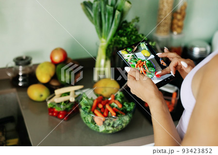 Close-up of a girl's hand taking a photo on her phone. A young woman, a culinary blogger, cooks in her home kitchen and takes photos on her smartphone. 93423852
