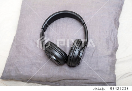 Stylish black headphones for listening to music lie on a small gray pillow in the bedroom. 93425233