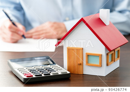 不動産契約書にサインする男性。テーブルの上の電卓と住宅模型。 不動産契約書にサインする男性。テーブルの上の電卓と住宅模型。 93426774