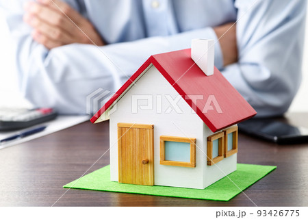 テーブルの上のに置かれた電卓と住宅模型。腕組みをして不動産に関することを考える男性。 93426775