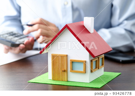 テーブルの上のに置かれた住宅模型と契約書。電卓で計算する男性。 93426778