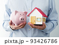 ブタの貯金箱と家の模型を持つ男性。家計の節約のイメージ。 93426786