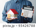 家の模型と電卓を持つ男性。価格を提示する男性のイメージ。 93426788