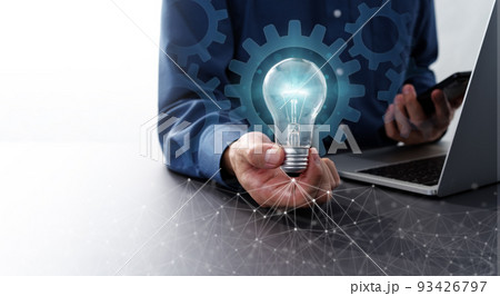 オートメーションテクノロジーとビジネスソリューションのイメージ。青く光る電球とスマートフォンを持つ男 93426797