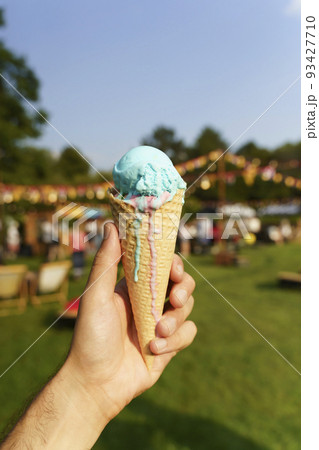 Ice cream cone in hand. Sweet dessert on summer picnic blurred background. Food, summer, ice cream concept. Selected focus Ice cream cone in hand. Sweet dessert on summer picnic blurred background. Food, summer, ice cream concept. Selected focus 93427710