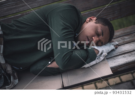Dark-skinned man sleeping on cardboard on bench 93431532