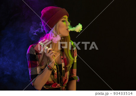 Vaping girl. Young hipster woman vape e-cig on black background. Hip-hop style. Studio shot Vaping girl. Young hipster woman vape e-cig on black background. Hip-hop style. Studio shot 93433514