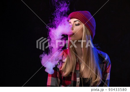 Vaping girl. Young hipster woman vape e-cig on studio on black background. Hip-hop style. Close up. Vaping girl. Young hipster woman vape e-cig on studio on black background. Hip-hop style. Close up. 93433580