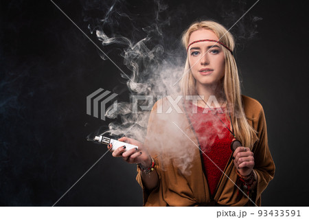 Portrait of sexy young hipster smoking vaping girl. The woman is dressed in the style of a boho. Vapor concept. Vaping e-Cigarette. Portrait of sexy young hipster smoking vaping girl. The woman is dressed in the style of a boho. Vapor concept. Vaping e-Cigarette. 93433591