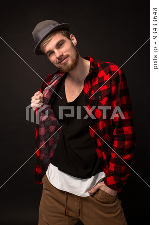 Handsome trendy young guy at the studio on black background. He wears beard and a plaid shirt Handsome trendy young guy at the studio on black background. He wears beard and a plaid shirt 93433648